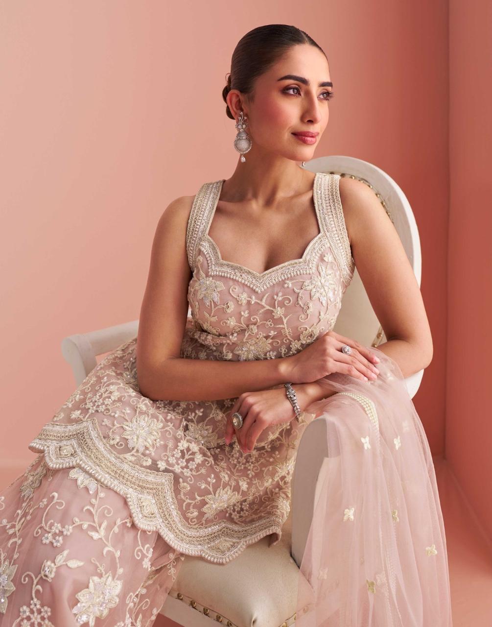 Model wearing a pink Sharara sitting on a chair in front of a rose gold background