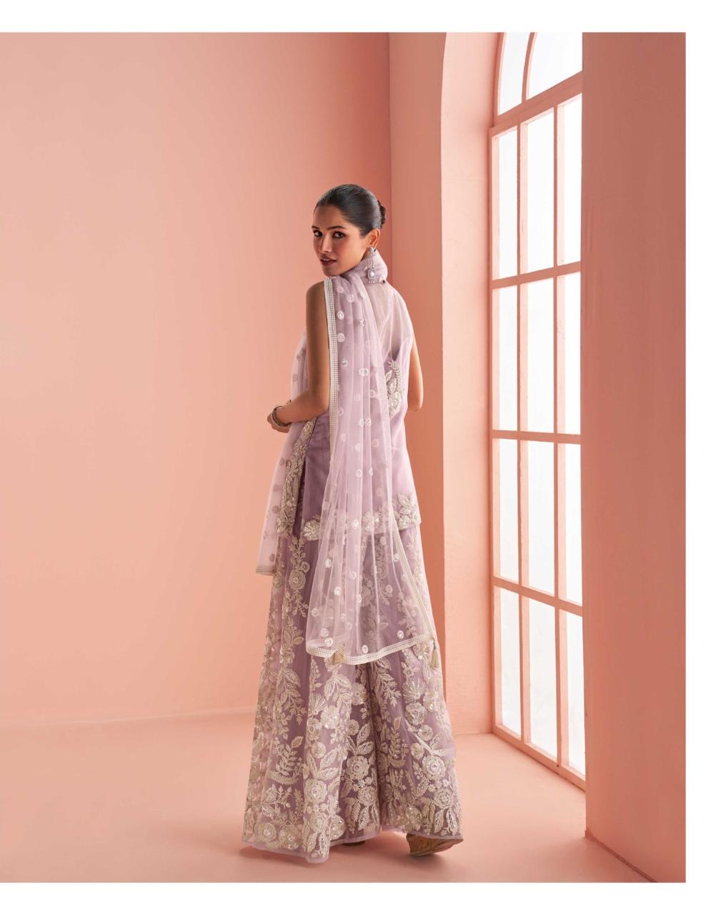 Model facing backwards wearing a pink floral sharara standing in front of a rose gold wall.