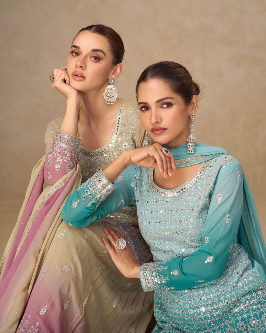 Two women in traditional embroidered outfits sitting against a beige background