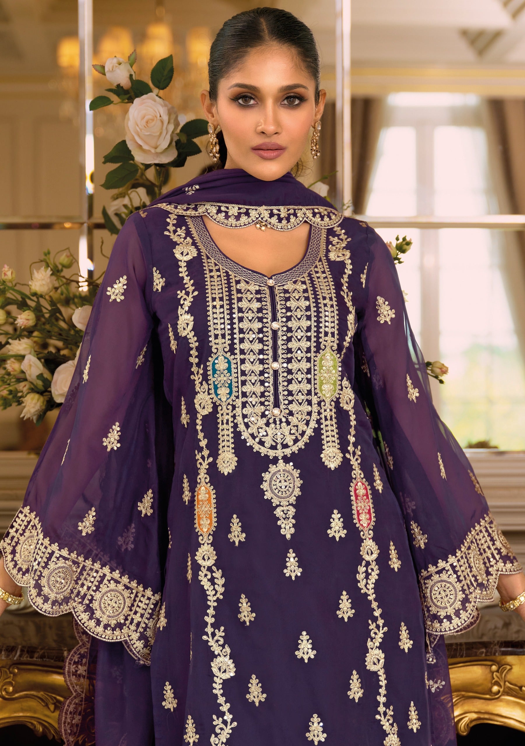 Woman wearing a purple embroidered traditional outfit in an elegant indoor setting.