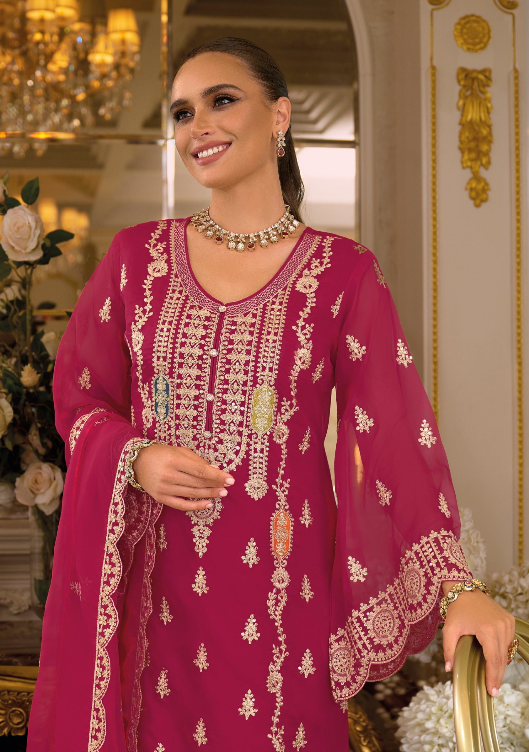 Woman in a pink embroidered traditional outfit with jewelry in an ornate interior setting