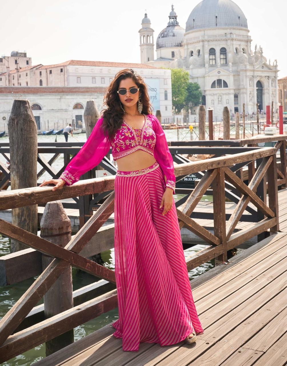 Woman in a pink traditional outfit standing on a wooden bridge with a scenic background