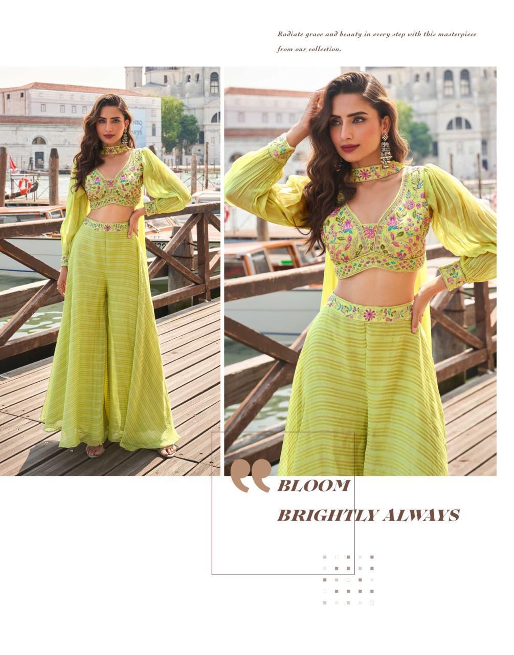 Woman in a bright yellow traditional outfit with floral patterns, standing on a wooden dock with water and buildings in the background.