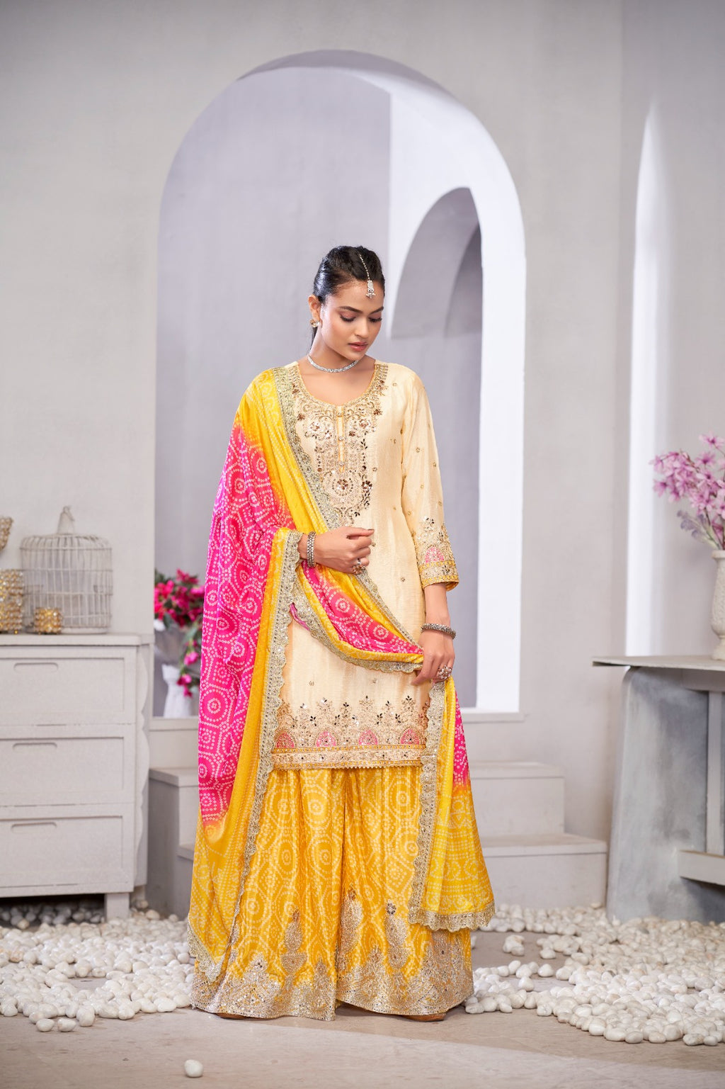 Woman in a traditional outfit with yellow and pink elements standing in a decorative room.