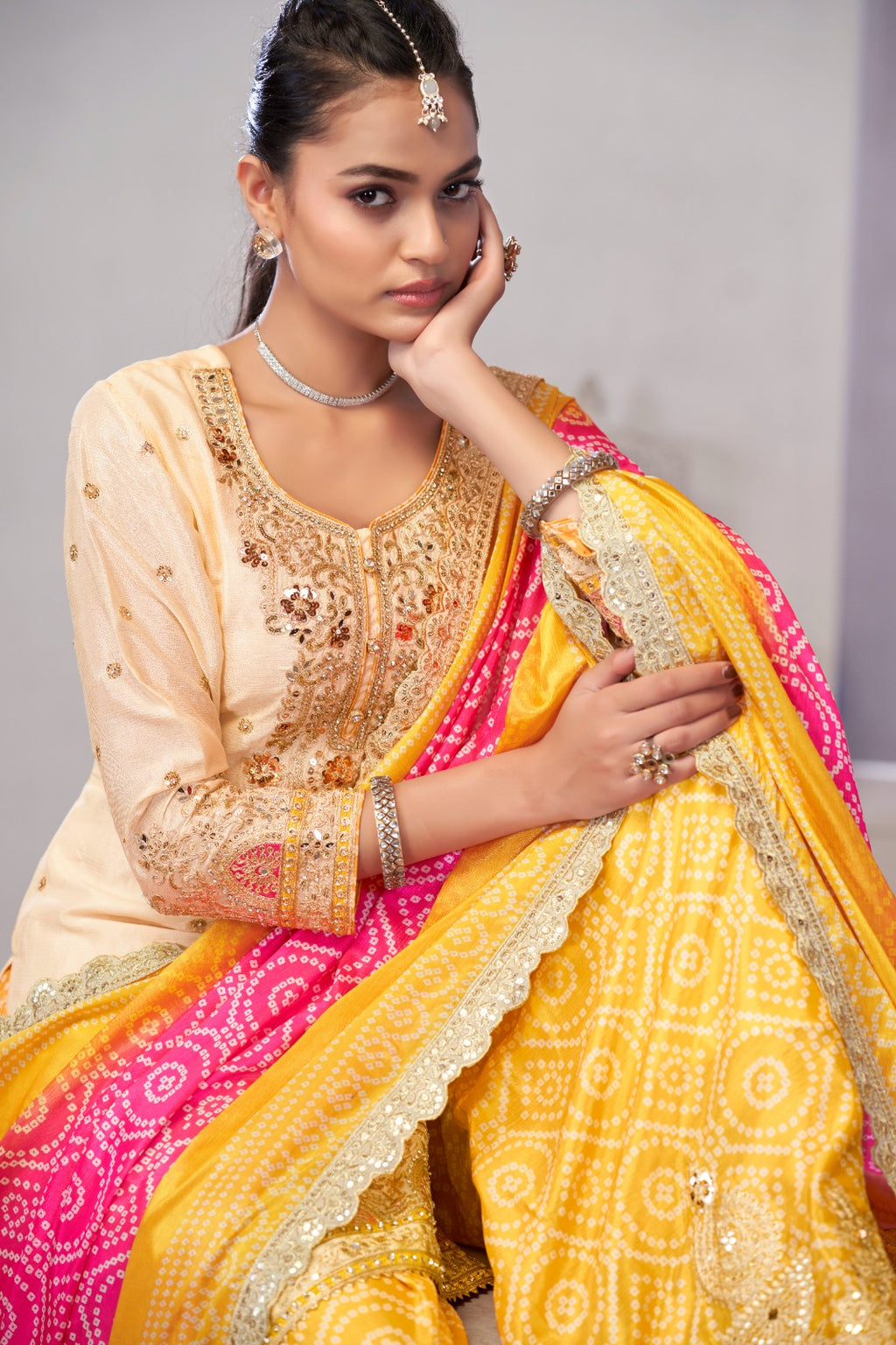 Woman wearing a traditional outfit with a yellow and pink saree and beige blouse.