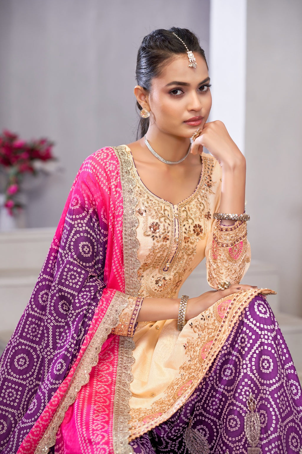 Woman in traditional Indian attire with a purple and pink saree, sitting indoors.
