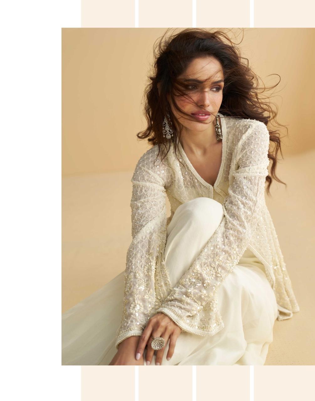 Woman in a white embroidered outfit sitting against a beige background