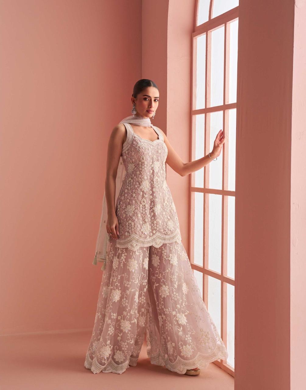 Woman in a floral outfit standing in a room with pink walls and a large window.