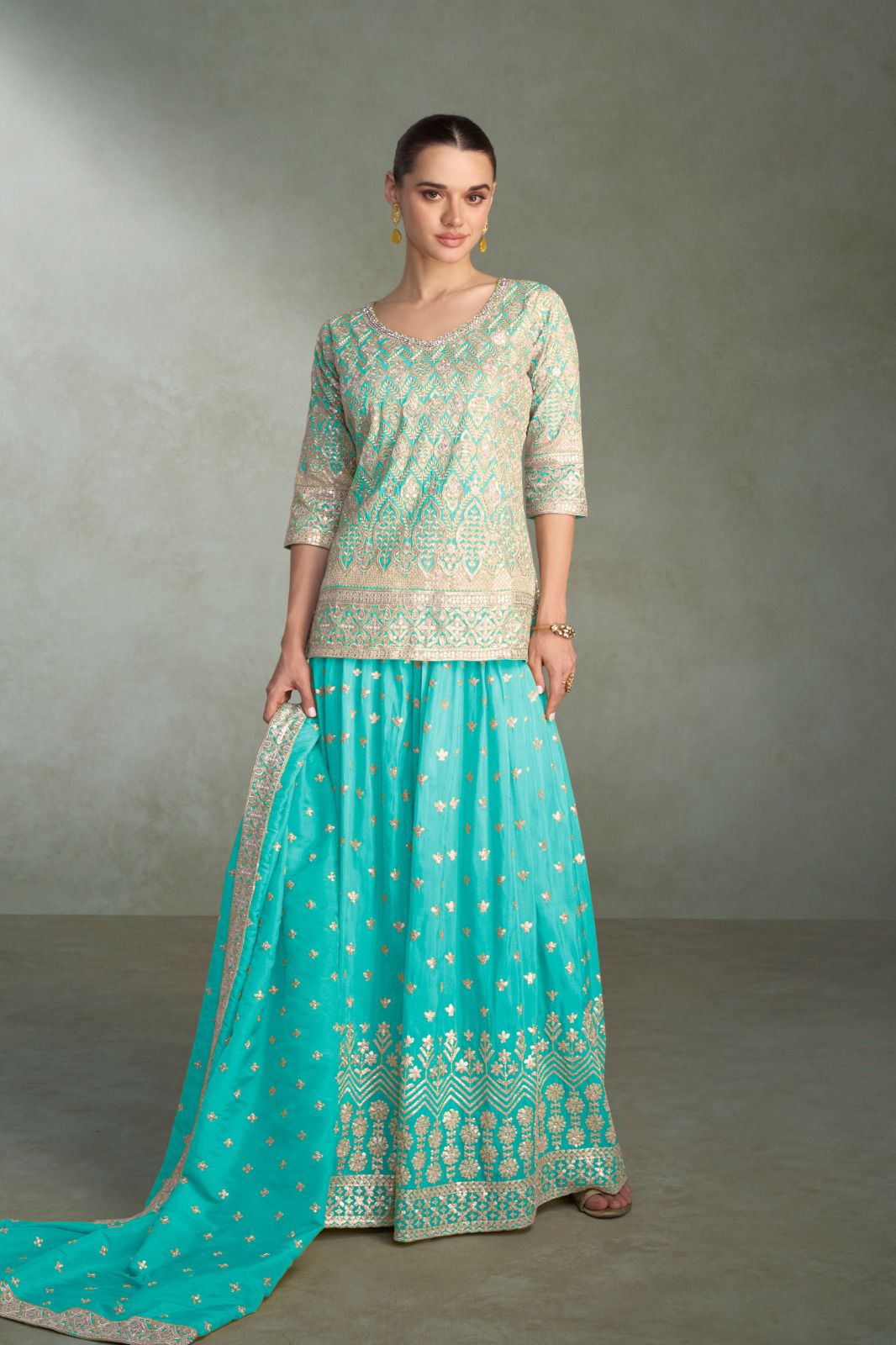 Woman wearing a traditional outfit with a green top and turquoise skirt against a gray background