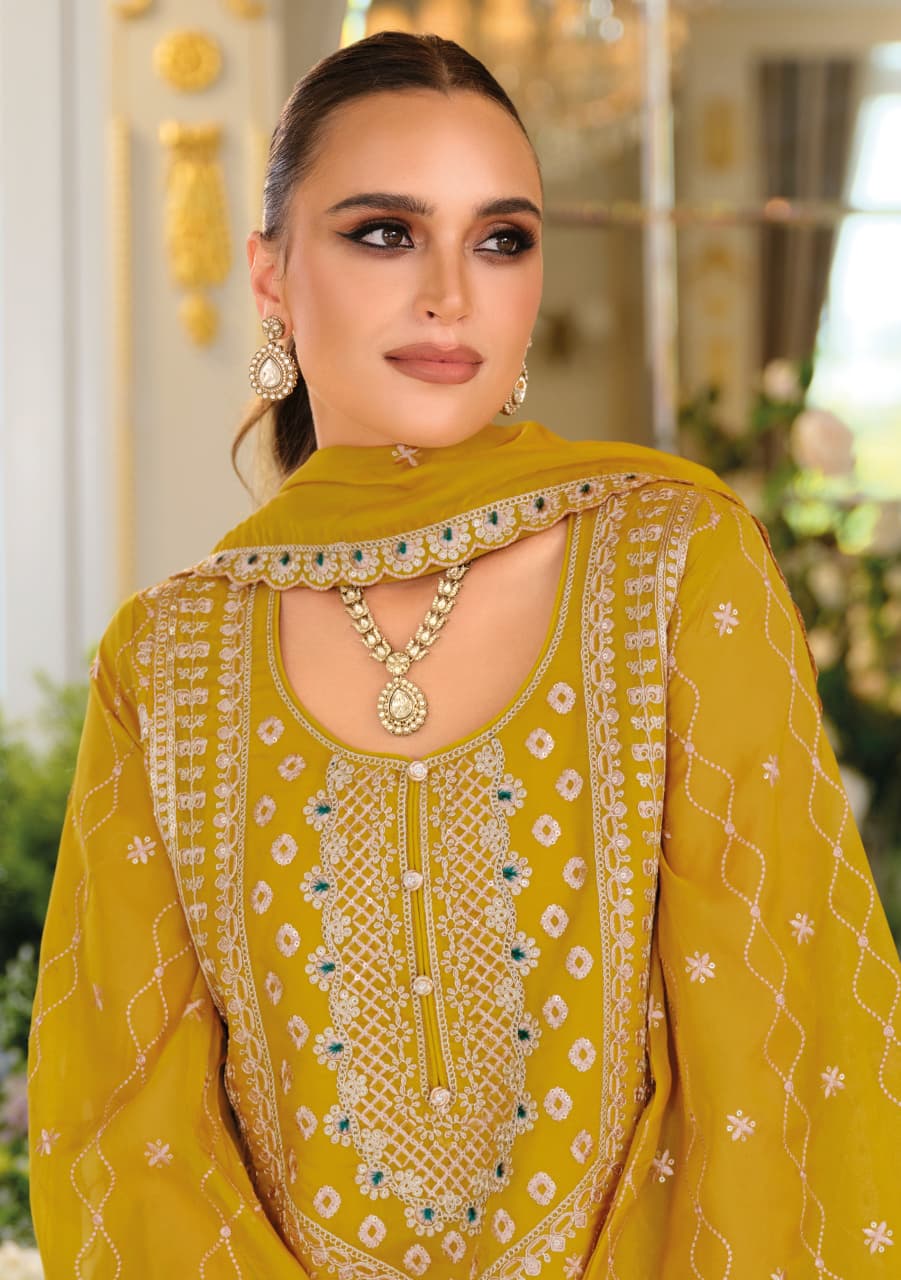 Woman wearing a mustard yellow embroidered outfit with jewelry indoors.