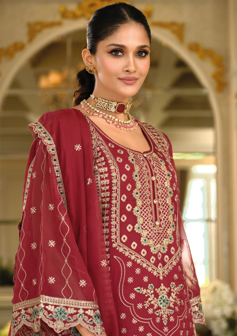 Woman wearing a maroon embroidered traditional outfit with gold jewelry indoors.