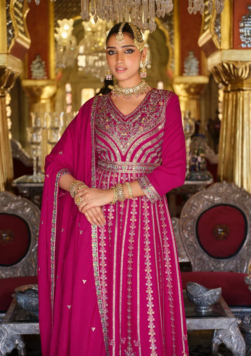 Woman in a pink traditional outfit with intricate designs in a decorated room.